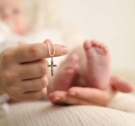Sacrament of baptism. Woman holding little baby and gold cross indoors, selective focusの写真素材