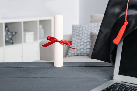 Diploma, graduation hat and laptop on gray wooden table indoors, selective focusの写真素材