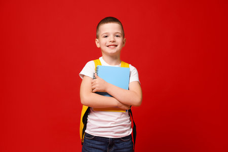 Cute little boy with backpack and notebooks on red backgroundの写真素材