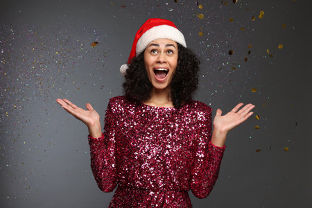 Happy woman wearing Santa hat and having fun on grey background with falling confetti. Christmas partyの写真素材