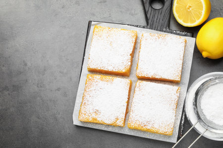 Tasty lemon bars with powdered sugar and fresh fruits on gray table, flat lay. Space for textの写真素材