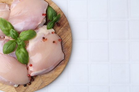 Raw chicken thighs with basil and peppercorns on white tiled table, top view. Space for textの写真素材