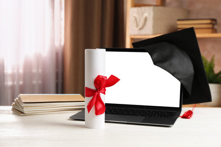 Diploma, graduation cap, stacked copybooks and laptop on white wooden table indoors, closeupの写真素材