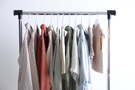 Different women's clothes hanging on rack against light backgroundの写真素材