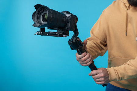 Videographer using gimbal stabilizer with camera on light blue background, closeupの写真素材