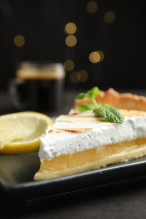 Slice of tasty lemon meringue tart with mint served on black table against blurred lights, closeupの写真素材