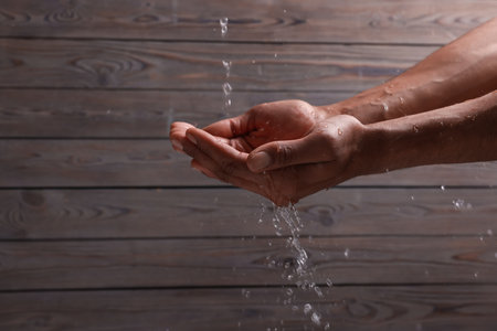 Pouring water into man's hands against wooden background, closeup. Space for textの写真素材