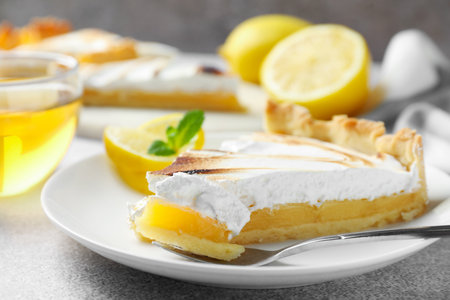 Slice of tasty lemon meringue tart with mint served on light gray table, closeupの写真素材