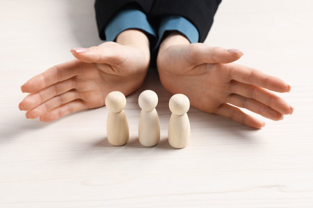 Woman protecting human figures at white wooden table, closeupの写真素材
