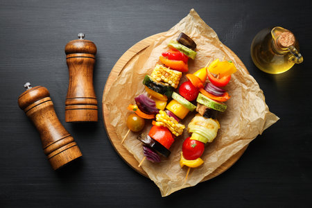 Salt, pepper shakers, oil and tasty grilled vegetables on black wooden table, flat layの写真素材