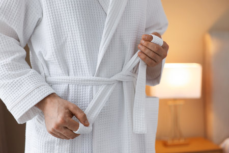 Man tying belt of bathrobe indoors, closeupの写真素材