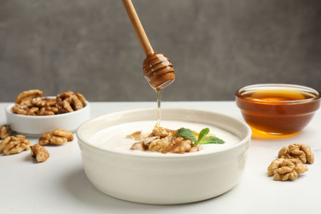 Dripping honey into Greek yogurt with walnuts and mint at white table, closeupの写真素材