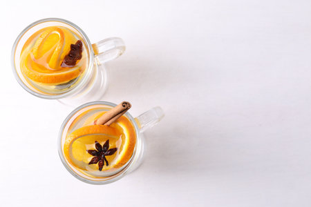 Tasty mulled wine with spices and orange slices in glass cups on white table, flat lay. Space for textの写真素材