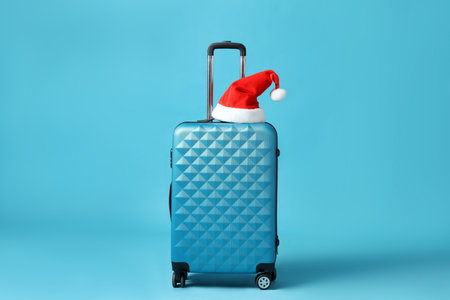 Santa hat on suitcase against light blue background. Christmas vacationの写真素材