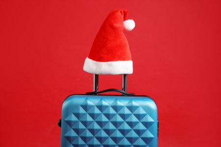 Christmas vacation. Blue suitcase with Santa hat on red backgroundの写真素材