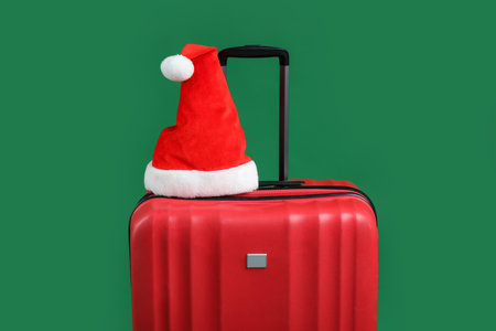 Santa hat on red suitcase against green background. Christmas vacationの写真素材