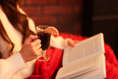 Woman with mulled wine reading book at home, closeupの写真素材