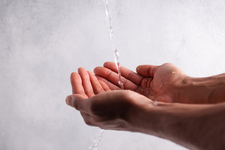 Pouring water into man's hands against light gray background, closeup.. Space for textの写真素材