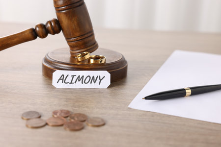 Paper note with word Alimony, judge's gavel, coins, wedding rings, pen and document on wooden table, closeupの写真素材