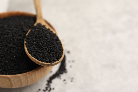 Aromatic black caraway in wooden bowl and spoon on light gray table, closeup. Space for textの写真素材