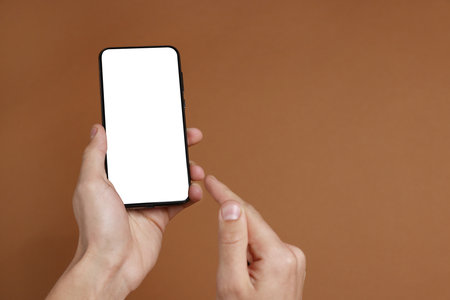 Man holding smartphone with blank screen on brown background, closeup. Mockup for designの写真素材