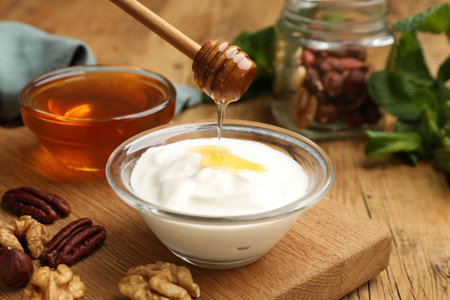 Dripping honey into Greek yogurt and nuts on wooden table, closeupの写真素材