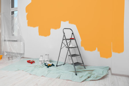Decorator's stuff in room. Wall partly painted in orange color. Interior renovationの写真素材