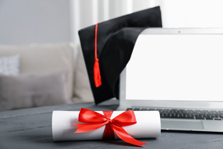 Diploma, graduation hat and laptop on gray wooden table indoors, selective focusの写真素材