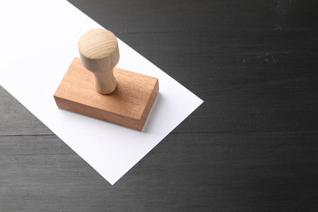 One wooden stamp and blank sheet of paper on black table. Space for textの写真素材