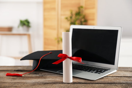 Diploma, graduation hat and laptop on wooden table indoors, selective focus. Space for textの写真素材