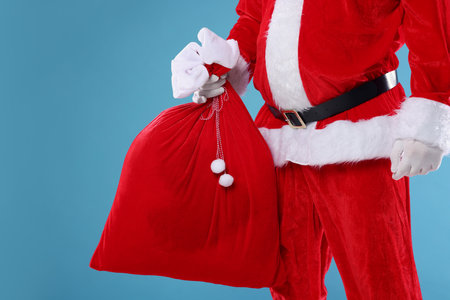 Santa Claus holding sack on light blue background, closeup. Merry Christmas and Happy New Yearの写真素材