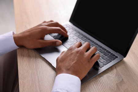 African-American man using laptop at wooden table indoors, closeupの写真素材