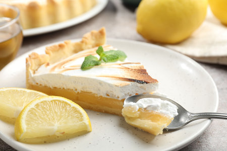 Slice of tasty lemon meringue tart with mint served on light gray table, closeupの写真素材