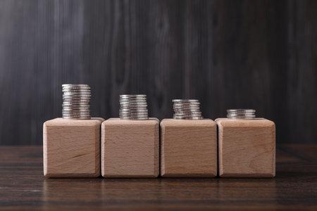 Empty cubes with stacked coins on wooden table against dark gray background. Space for design