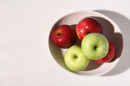 Fresh red and green apples with water drops in bowl on white table, top view. Space for textの写真素材