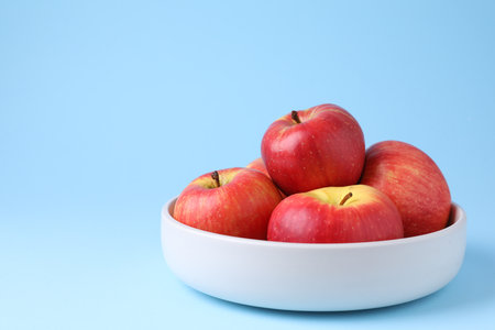 Ripe red apples in bowl on light blue background, closeup. Space for textの写真素材