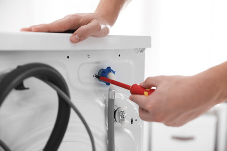 Repairman fixing broken washing machine with screwdriver at home, closeupの写真素材