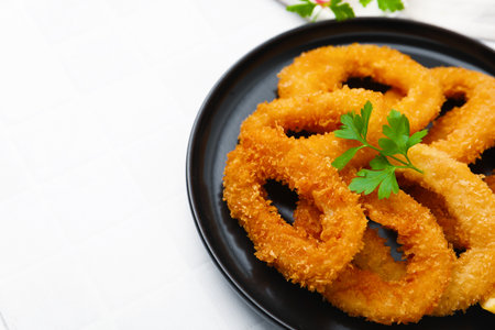 Deep fried squid rings with parsley on white tiled table, closeup. Space for textの写真素材