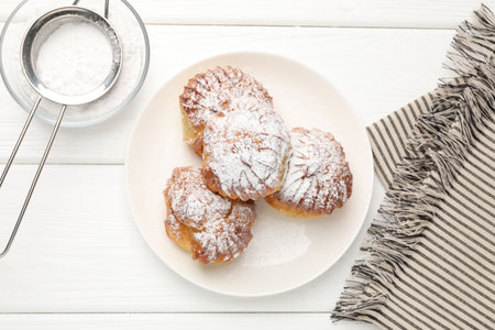 Tasty profiteroles with powdered sugar on white wooden table, flat lay