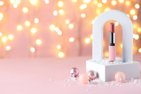 Stylish presentation of lipstick and Christmas baubles on pink table against blurred lights, closeup. Space for textの写真素材