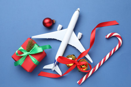 Christmas vacation. Toy plane, gift box, candy cane, jingle bells and bauble on blue background, flat layの写真素材