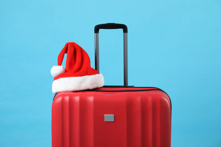 Santa hat on red suitcase against light blue background. Christmas vacationの写真素材