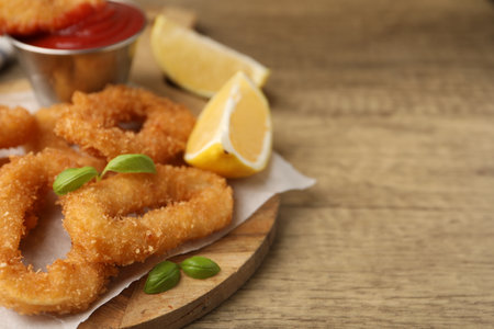 Deep fried squid rings with lemon slices, basil on wooden table, closeup. Space for textの写真素材