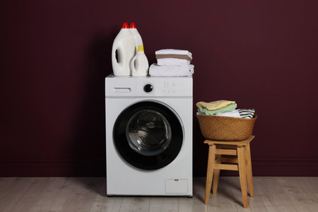 Modern washing machine, detergents and clothes near burgundy wall indoorsの写真素材