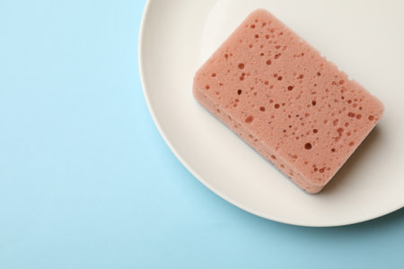 Kitchen sponge and plate on light blue background, top view. Space for textの写真素材