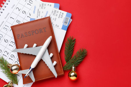 Christmas vacation. Passport with tickets, toy plane, calendar, fir branches and baubles on red background, flat lay. Space for textの写真素材