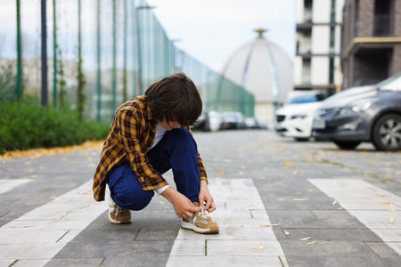 Little boy tying shoelaces on pedestrian crossing outdoors, space for text. Child in danger and road safetyの写真素材