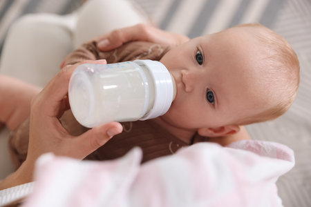 Mother feeding her little baby with bottle at home, above view