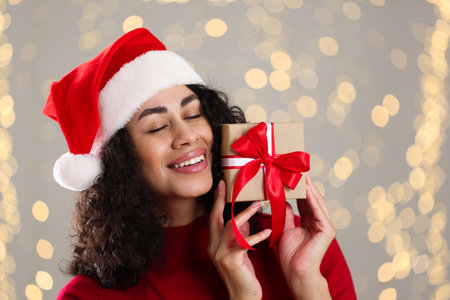 Portrait of attractive woman with Santa hat and Christmas gift against blurred lights