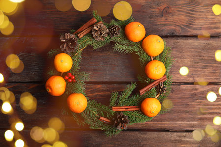 Christmas wreath with tangerines, fir tree branches, cones and cinnamon sticks on wooden wall. Bokeh lightsの写真素材